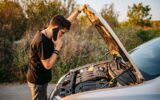 Adult looking at open hood of car and calling roadside assistance